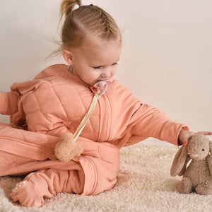 Adorable toddler in a dusty pink quilted onesie sleep suit with little bunny doll